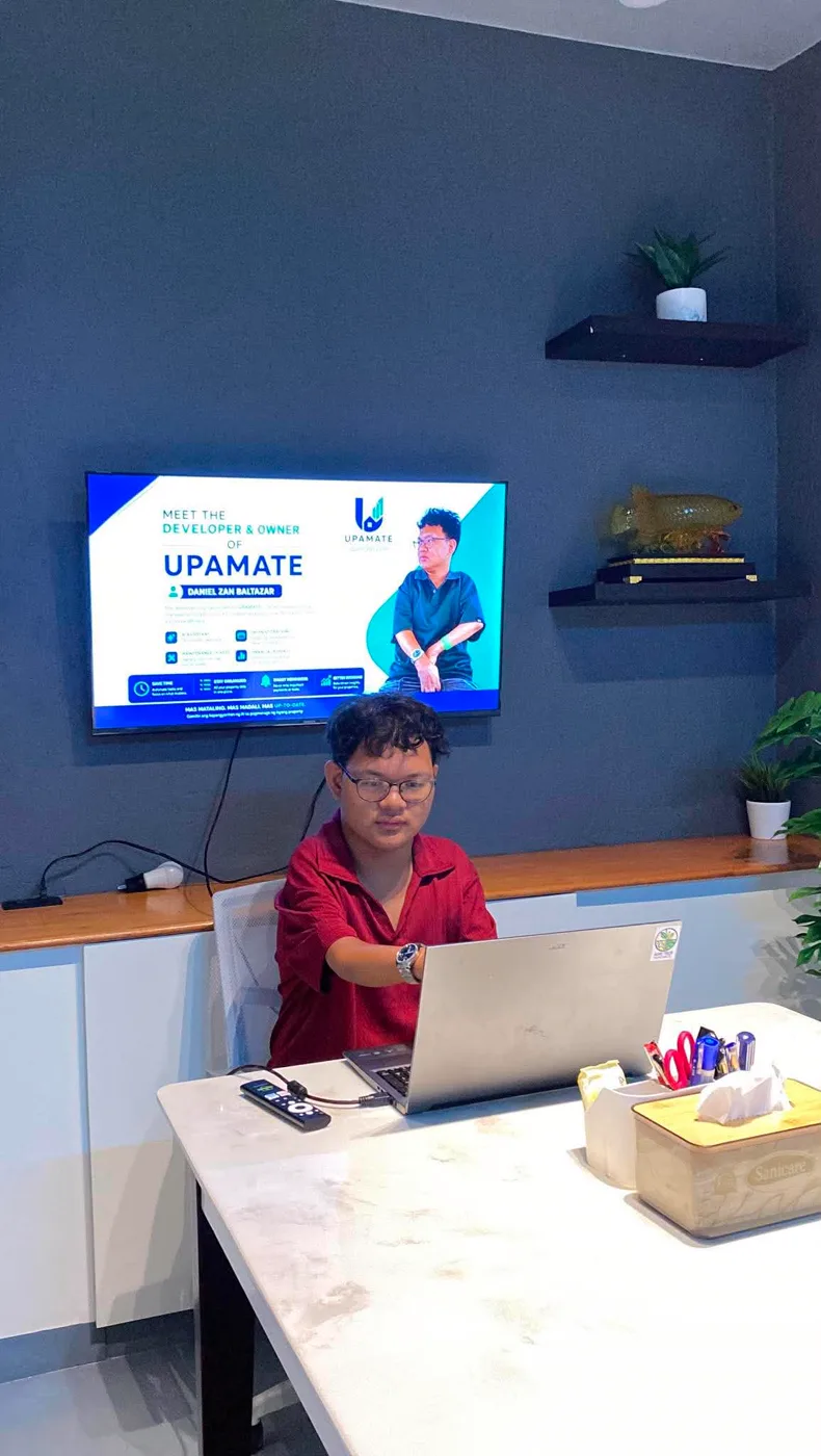 Daniel at a desk under a screen that reads Meet the developer and owner of UPAMATE